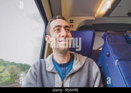 Junger Mann auf Reisen in einem Zug und lächelnd an jemand Stockfoto