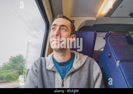 Junger Mann auf Reisen im zug und schaut aus dem Fenster und Lächeln Stockfoto