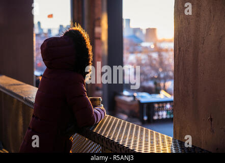 Frau mit Pelz hoodie Kaffee trinken und beobachten den Sonnenuntergang von New York Highline Stockfoto