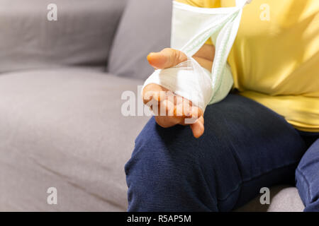 Ältere Frau sitzt auf einem Sofa mit Hand verletzt auf einem Gipsverband. Stockfoto