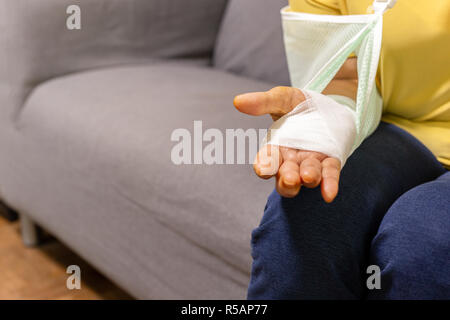 Ältere Frau sitzt auf einem Sofa mit Hand verletzt auf einem Gipsverband. Stockfoto