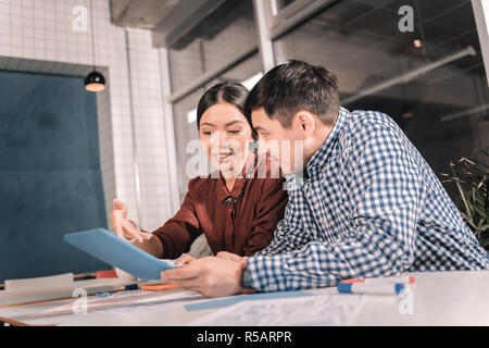 Dunkelhaarige Mann mit squared Shirt in der Nähe seiner weiblichen Kollegen sitzen Stockfoto