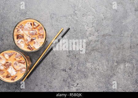 Kalt Eiskaffee in hohes Glas mit Schwarz und Gold Pailletten auf grauem Beton Hintergrund gebraut. Schokolade, Vanille, Karamell oder Zimt Eiskaffee in t Stockfoto