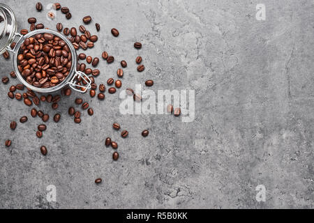 Kaffee Bohnen im Glas von Kaffeebohnen auf grauem Beton Hintergrund umgeben. Ansicht von oben mit der Kopie Platz für Text. Stockfoto