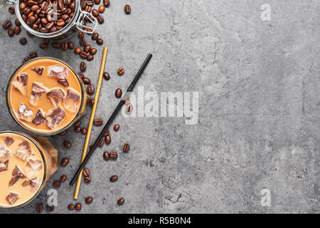 Schokolade, Vanille, Karamell oder Zimt Eiskaffee im großen Glas. Kalt Eiskaffee in Glas und Kaffeebohnen in Glas Glas auf grauem Beton bac gebraut Stockfoto