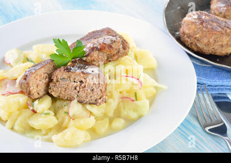 Bayerische hausgemachte Frikadellen von Rind- und Schweinefleisch, gebraten in eine eiserne Pfanne, auf hausgemachte patato Salat mit Gurke und Radieschen serviert. Stockfoto