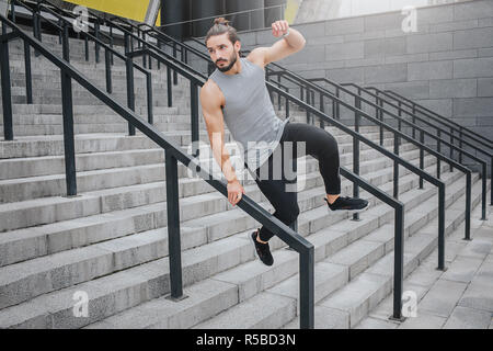 Junge Mann in Bewegung ist. Er hält eine Hand auf Barriere und springt über. Er sieht gerade. Junger Mann springt auf Treppen. Er ist zuversichtlich und erfahrenen Stockfoto