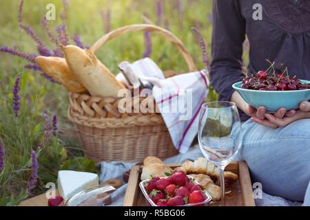 Sommer - Mädchen beim Picknick auf der Wiese. Käse Brie, Baguette, Erdbeere, Kirsche, Wein, Croissants und Korb Stockfoto