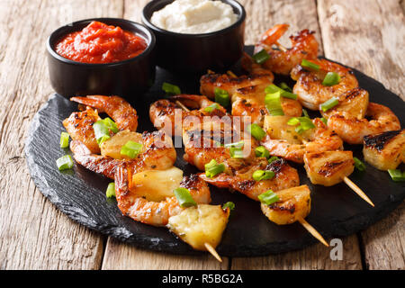 Feine Vorspeise von Kebab gegrillte Shrimps und Scheiben Ananas serviert mit Saucen close-up auf einer Schiefertafel Platte auf einem Holztisch. Horizontale Stockfoto