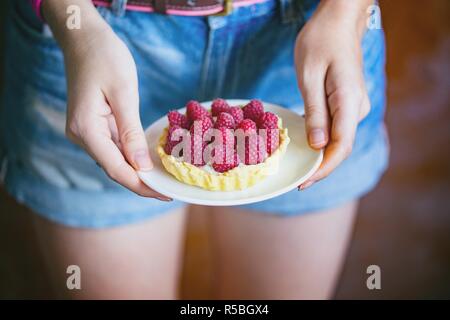 Das Mädchen hält in ihrer Hände lecker, nützliche und schöne Törtchen mit Himbeeren Stockfoto