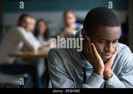 African American tausendjährigen Kerl einsam allein sitzen im Cafe, beleidigt schwarzen Studenten vermeiden Gespräch mit Freunden, in der es an Unverständnis, junger Mann Stockfoto