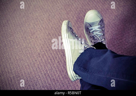 Füße in Blue Jeans mit weißen - gekreuzte ish Sneakers auf dem Fußboden; Copy-Raum zur Verfügung. Stockfoto