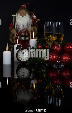 Zwei Weingläser mit Champagner, Santa Claus, Uhr, Kerzen und Weihnachten Geschenke auf einem schwarzen Hintergrund mit Reflexion. Kopieren Sie Platz. Frohe Weihnachten ein Stockfoto