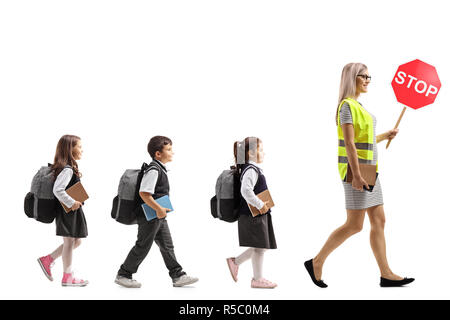 Volle Länge Profil Aufnahme von Schülern zu Fuß hinter einer Lehrerin mit einer Warnweste und ein Stop-Schild auf weißem Hintergrund Stockfoto