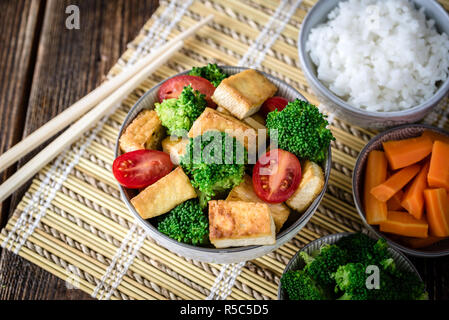 Gegrillter Tofu mit Brokkoli und Tomaten in Weiß Schüssel auf Bambus Pad mit Stäbchen auf der linken Seite. Stockfoto