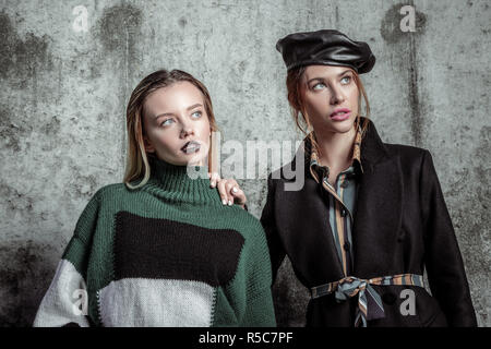 Schönes Make-up. Zwei junge vielversprechende Frauen mit schönen Make-up in neuen Kleidern posiert in der Nähe der graue Wand Stockfoto