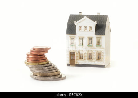 Stapel von Münzen neben einem Miniatur Altbau Haus, Immobilien Konzept für Eigenschaft Investition oder Mietkosten für ein Haus, auf einem weißen Bac isoliert Stockfoto