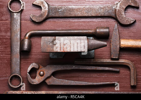 Alten rostigen robuste Amboss und andere Schmied Werkzeuge auf Braun Natur Holz- Hintergrund. Flach Ansicht von oben. Stockfoto