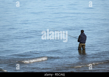 Anonyme junger Mann von hinten steht im Wasser der Ostsee und hält eine Angelrute in seinem Abenteuer Urlaub in der Natur, kopieren Raum Stockfoto