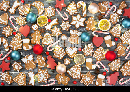 Weihnachten Muster aus Lebkuchen cookies, Anis Sterne, allspices, Beeren, Zuckerstange Lutscher, Weihnachtskugeln, orange Chips und Holzdekorationen mit Girlande auf Holz- Hintergrund. Flach. Stockfoto