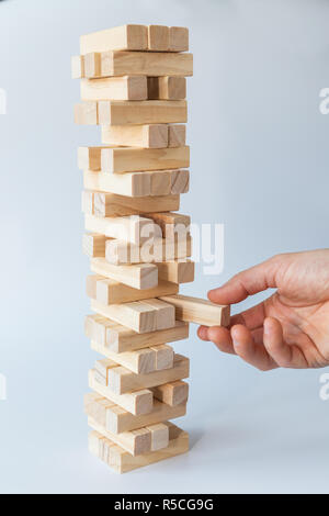 Hand des Menschen nehmen oder einen Block zu einer instabilen und unvollständige Turm von Holzblöcken. Konzept Foto von Planung, Risiken und strategische Planungen. Stockfoto