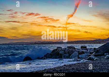 Sonnenuntergang über der Baie des Anges und die Promenade des Anglais: Wellen und Felsen am Strand in Nizza Provence Cote D'Azur Frankreich Stockfoto