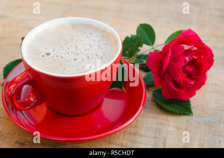 Rot Tasse Kaffee oder Cappuccino und Rose auf Holz- rustikalen Tisch von oben, Frühstück am Muttertag, Tag der Frauen oder Valentines Tag Stockfoto