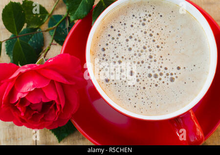 Rot Tasse Kaffee oder Cappuccino und Rose auf Holz- rustikalen Tisch von oben, Frühstück am Muttertag, Tag der Frauen oder Valentines Tag Stockfoto