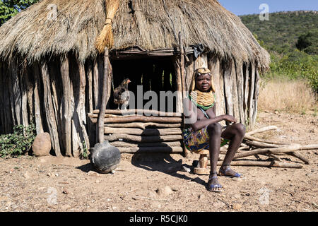Portrait einer jungen Muila Mädchen sitzt vor ihrer Hütte, während ein Huhn im Inneren ist. Stockfoto