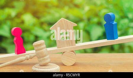 Aufteilung des Eigentums mit rechtlichen Mitteln. Klärung des Eigentums an dem Haus. holzfiguren von Menschen. Mann und Frau auf der Waage stehen. Tria Stockfoto
