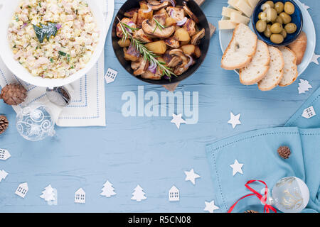 Verschiedene traditionelle Speisen für Tabelle zum Neuen Jahr. Russischer Salat, Gebäck, Häppchen und Bratkartoffeln mit Pilzen. Ansicht von oben. Freier Speicherplatz für c Stockfoto