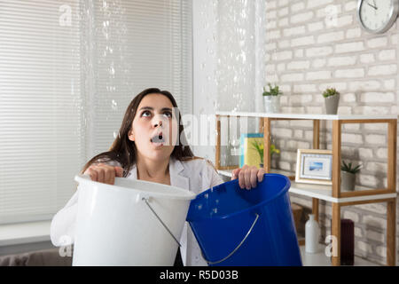 Frau Sammeln austretendes Wasser im Eimer Stockfoto