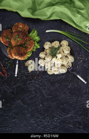 Gebratene Schnitzel und russischen Pelmeni auf schwarzem Hintergrund Stockfoto