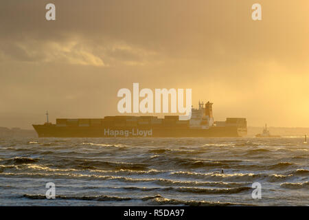 Container; Frachtschiff Hapag-Lloyd steuert nach turbulenten Tagen auf See in den Hafen und Hafen. Crosby, Merseyside, 30. November 2018. Starke Winde an der Uferpromenade der Mersey-Mündung, wenn die Sonne an einem stürmischen Tag untergeht. Sonnenschein und Duschen über dem Fluss Mersey und den walisischen Hügeln, während der Sturm Diana nachlässt. Stockfoto