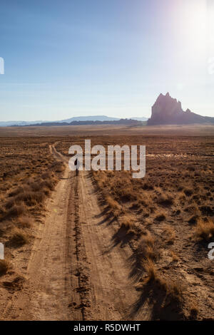 Frau, die zu Fuß auf einem Feldweg in der trockenen Wüste mit einem Berg im Hintergrund. Bei Shiprock, New Jersey, USA. Stockfoto