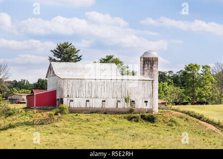 Ein großes, weißes Vieh Scheune mit Silo steht auf einem hügeligen Ohio Farm unter einem bewölkten Himmel. Stockfoto