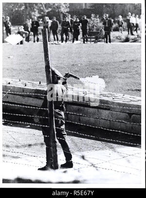 Oktober 1961-kommunistischen "Polizisten" (volkspolizist), stehen zwischen den Grenzzaun und Wand, bereitet eine Tear-Gas Granate bei einer Gruppe von West-berliner, die auf Ihrer Seite der Grenze versammelt die Roten Garden zu Jeer zu werfen Stockfoto