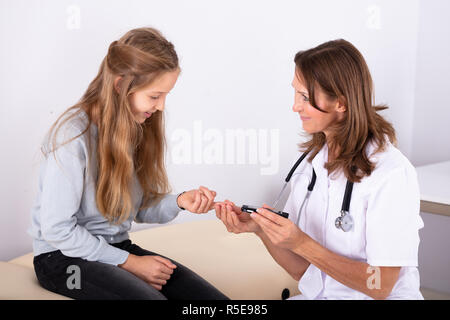 Ärztin überprüfen Smiling Girl's Patient Blutzuckerspiegel mit Glucometer in Klinik Stockfoto