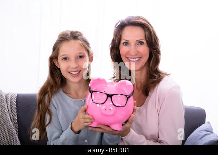 Portrait von lächelnden Mutter und Tochter Holding rosa Sparschwein Stockfoto