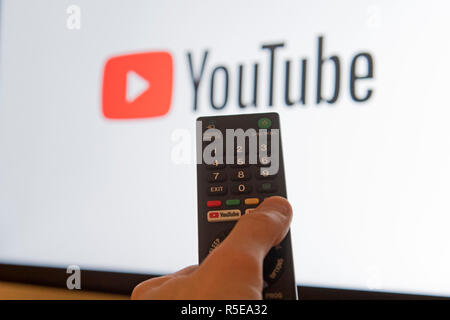 Ein Mann Punkte eine Fernbedienung auf ein intelligentes Fernsehen Anzeige der YouTube App in einem Schlafzimmer zu Hause in Großbritannien. November 2018.