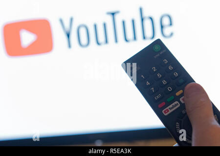 Ein Mann Punkte eine Fernbedienung auf ein intelligentes Fernsehen Anzeige der YouTube App in einem Schlafzimmer zu Hause in Großbritannien. November 2018. Stockfoto