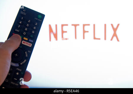 Ein Mann Punkte eine Fernbedienung auf ein intelligentes Fernsehen Anzeige der Netflix App in einem Schlafzimmer zu Hause in Großbritannien. November 2018.