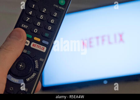 Ein Mann Punkte eine Fernbedienung auf ein intelligentes Fernsehen Anzeige der Netflix App in einem Schlafzimmer zu Hause in Großbritannien. November 2018. Stockfoto