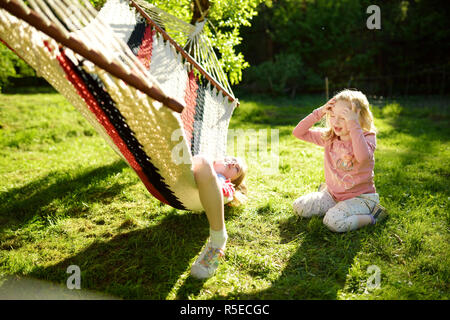 Süße kleine Schwestern Spaß in Hängematte auf schönen Sommertag. Kinder entspannen im Frühling Garten. Familie Freizeitaktivitäten im Sommer. Stockfoto