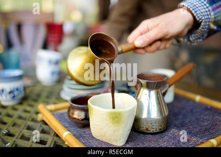 Gießen frischen heißen Kaffee aus einer Kupfer cezve in Keramik Schale in der gemütlichen Küche. Bunte Keramik Tassen und frischem heißem Kaffee. Vorbereitung köstlichen Kaffee Stockfoto