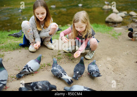 Zwei süße kleine Schwestern Fütterung Vögel auf Sommertag. Kinder füttern Tauben und Enten im Freien. Aktive Freizeit mit Kindern. Stockfoto