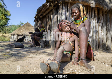 Muila Frau sitzt auf dem Boden, auf der Suche nach Parasiten auf den Kopf ihres jungen Tochter, während eine andere Frau ist gerade aus der Ferne. Stockfoto