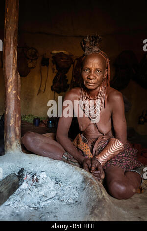 Porträt eines alten Himba Frau sitzt auf dem Boden ihrer Hütte neben dem Feuer. Stockfoto