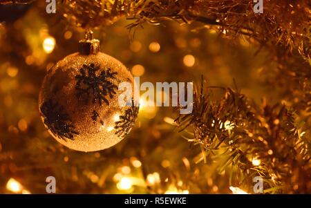 Nahaufnahme einer Weihnachtskugel hängen an einen Weihnachtsbaum mit einem schönen goldenen Glanz umhüllt das ganze Bild. Stockfoto