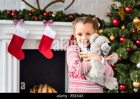 Adorable glückliches Kind umarmen Teddybären und an der Kamera zu Weihnachten lächelnd Stockfoto